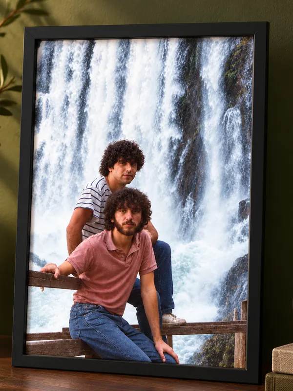 Cuadro con marco negro, con la foto restaurada de dos hermanos frente a una cascada